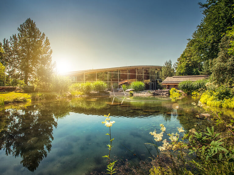 Ein natürlicher Badesee in Bodenmais glänzt im Schein der Sonne am Himmel.