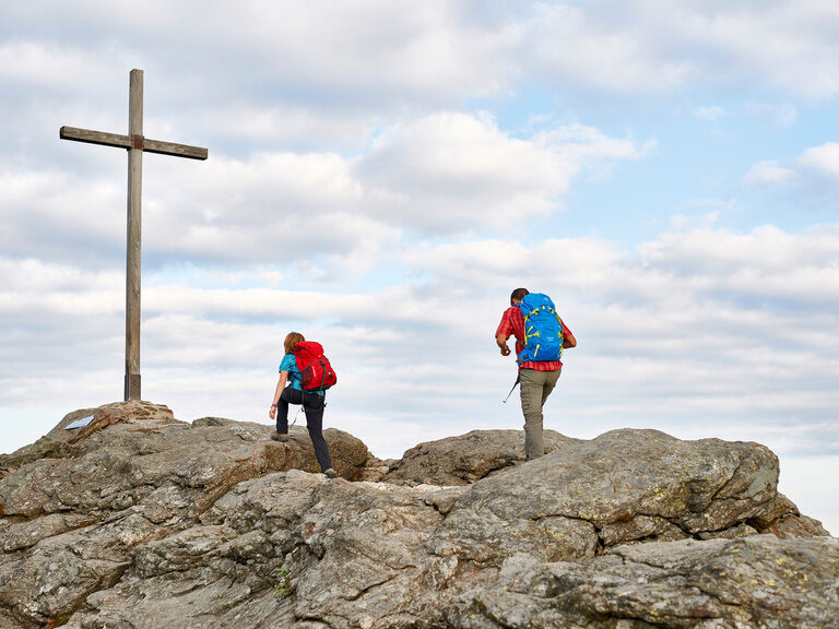 Zwei Personen wandern bei perfekten Wanderwetter zum Gipfelkreuz.