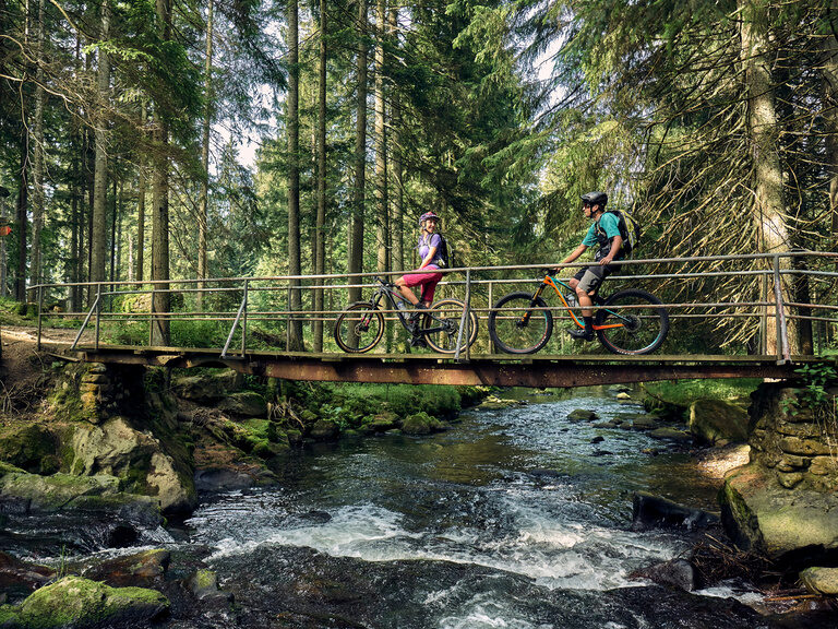 Naturerlebnis mit dem Fahrrad: kurze Pause auf einer Brücke im Wald über einem Flusslauf bei Bodenmais